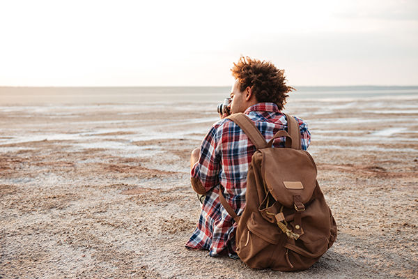 Man with backpack sitting on the beach at dawn.