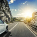 White car on a mountain road. The sun is shining and the sky is clear.