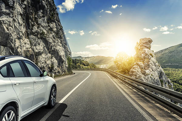 White car on a mountain road. The sun is shining and the sky is clear.