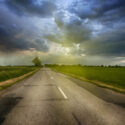 Road on a cloudy day with sunshine peeking out behind the clouds