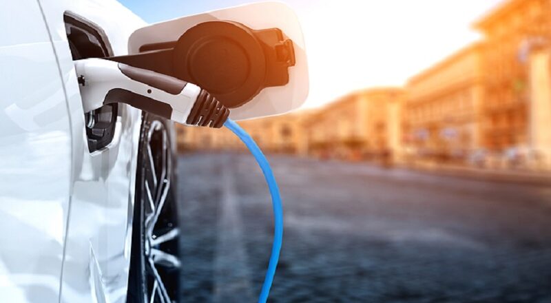 Electric car charging at sunset in a city.